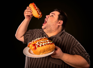 Diet failure of fat man eating fast food hot dog on plate. Breakfast for overweight person who greedily eats lot. Use of semi-finished products for food. Enraged by large amount of food fat.