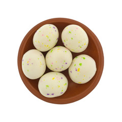 Top view of white speckled Easter egg malt ball candies in a small red clay bowl isolated on a white background.