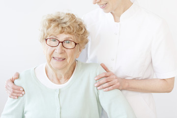 Smiling assistant hugging old lady