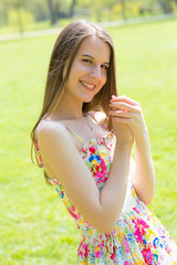 Portrait of young beautiful woman with long hair wearing flower dress in green spring park