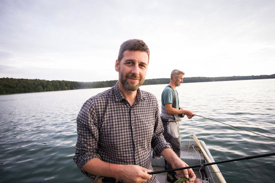 Caucasian men are fly fishing in boat on lake.