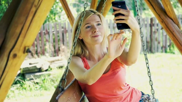 Young, pretty woman taking selfie photo sitting on the swing in the garden
