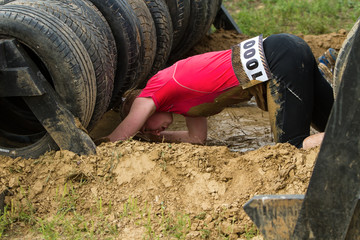 The girl creeps in the mud, emotionally overcoming the obstacle made of tires.