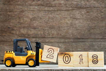 Toy plastic forklift hold block to compose and fulfill wording 2018 on wood background