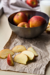 Fresh red apples in a stylish iron dish lying on a white window sill. Apple slices and a glass of milk are used as decoration.