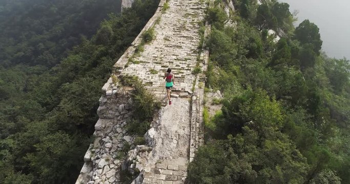 aerial view of young fitness woman trail runner running on top of great wall