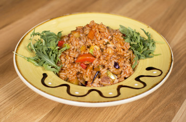 A plate of rice with vegetables. Appetizing healthy rice with vegetables in white plate on a wooden background.