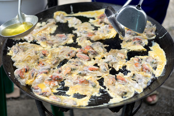 Cooking fried oyster omelet in big hot pan. Street restaurant in Thailand