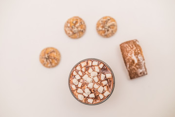 Glass of hot cocoa with marshmallows on table with cakes, view top
