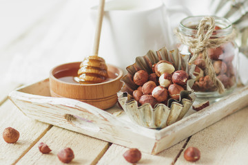 Honey in the wooden bowl, hazelnuts and jar with milk on the wooden tray