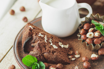 Piece of chocolate cake, mint leaves, hazelnuts and jar with milk