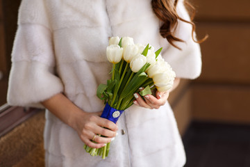 Winter wedding. Bride in white fur coat holding bouquet of fresh winter or spring flowers.