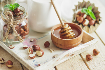 Honey in the wooden bowl, mint leaves, hazelnuts and jar with milk on the wooden tray