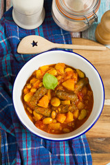 Butternut squash, pumpkin and bean stew with beef sausages. White bowl, dark blue tablecloth, wooden board.