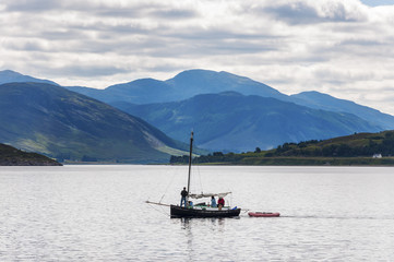 Fototapeta na wymiar Ullapool, Scotland - August 15, 2010: People in a small sailing boat in front of the small village of Ullapool in the Highlands in Scotland, United Kingdom