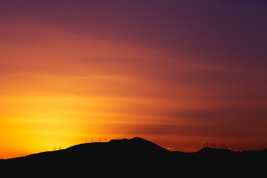 Mountain Ridge with Windmills over a Dark Red Sunset