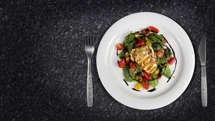 Grilled Halloumi Cheese poured with garlic olive oil salad witch grilled eggplant, cherry tomatoes, black olives and spinach. healthy food. Top view on granite kitchen countertop. Copy space added.