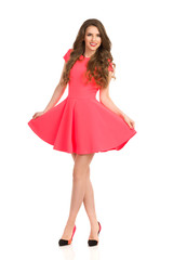 Smiling Woman In Pink Mini Dress Is Standing With Legs Crossed