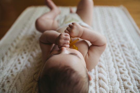 Cute young baby lying on blanket on floor - holding soother