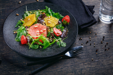 Grapefruit and orange mix salad with pine nuts on black plate and dark background