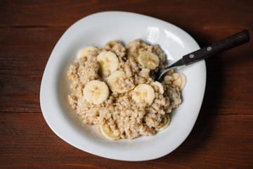 Oatmeal with banana and honey in white plate over wooden background