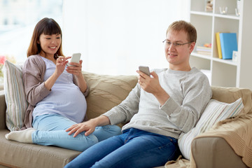 Obraz na płótnie Canvas husband and pregnant wife with smartphone at home