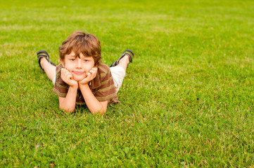Pensive little boy lies on a lawn