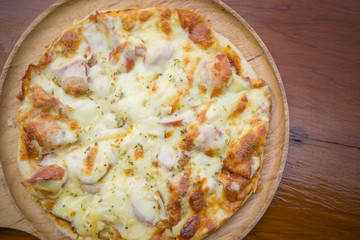 hawaiian pizza with cheeze on top in wood trey on wood table