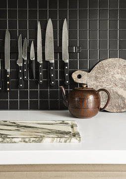 Kitchen knives hanging on the wall next to chopping board and tea pot