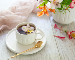 Obraz na płótnie Canvas White cup with tea on the table. Flowers nearby