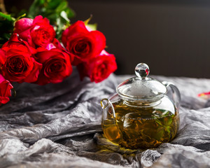 Obraz na płótnie Canvas Glass teapot on a dark background. Red Roses nearby