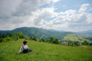 Naklejka na ściany i meble A boy sitting at the top of the hill and looking on mountains
