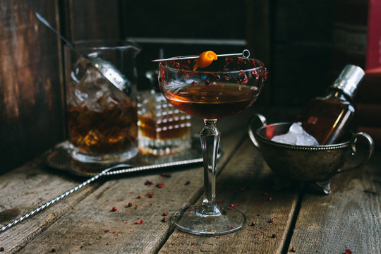 classic manhattan cocktail with orange peel and red pepper rim on wooden board