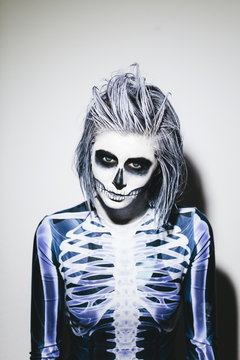 Spooky portrait of woman with skeleton costume and halloween make up on white wall