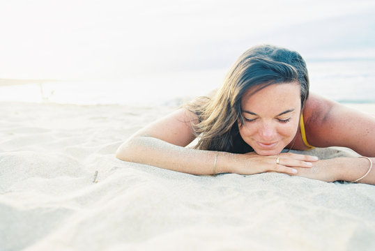 brunette woman in sand smiling on beach with ocean on film
