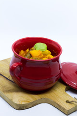 Butternut squash, pumpkin and bean stew with beef sausages. Red pot, white background. Isolated.