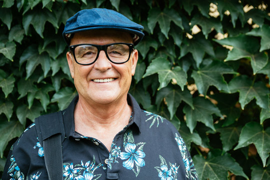 Hipster senior man portrait smiling with a beret and glasses in front of an ivy background
