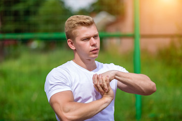 Stretches the muscles of the teams. The coach man does the warm-up, in the city on the nature, in the summer in a T-shirt. Athlete in nature. The concept of a healthy lifestyle. Exercise in the fresh © byswat