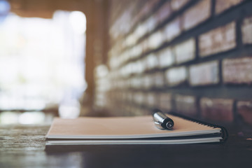 A blank white notebook and silver color pen on wooden table with brick wall background