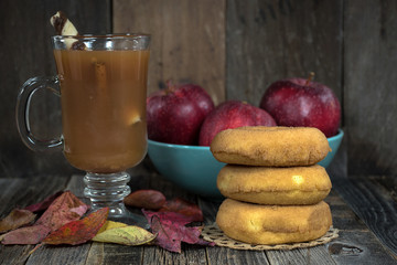 apple cider and donuts with autumn leaves and red apples on rustic wood
