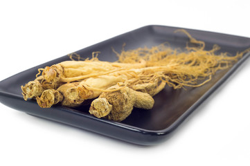 Ginseng root on the black plate isolated in white background.