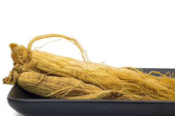 Ginseng root on the black plate isolated in white background.