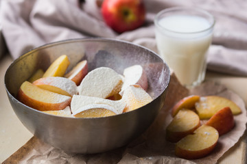 Fresh red apples sprinkled with flour in a stylish iron dish lying on a white window sill. Apple slices and a glass of milk are used as decoration.