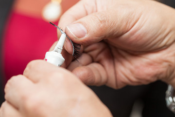 Close up of a make up artist hands applying cosmetic glue on fake eyelashes