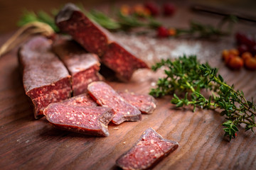 dry-cured salami sliced on wooden background with grapes and herbs