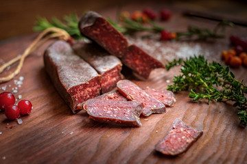 dry-cured salami sliced on wooden background with grapes and herbs
