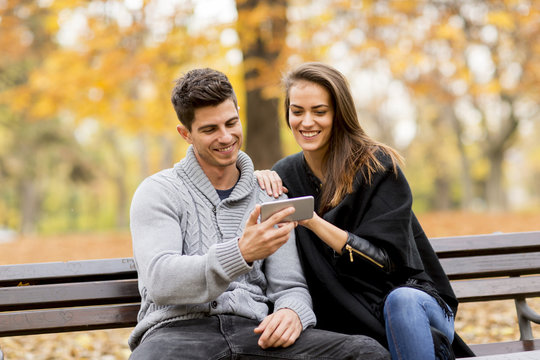 Young couple happily watching something on a smartphone and sitting on bench