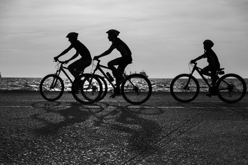 A family riding the bicycles together near the beach. Black and white silhouette