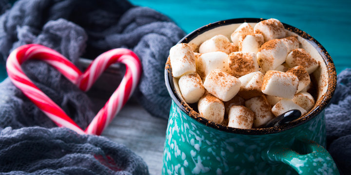 Hot chocolate with marshmallows on green background. Christmas winter still life with red candy canes in heart shape