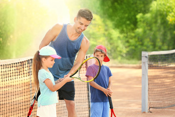 Young trainer with little children on tennis court